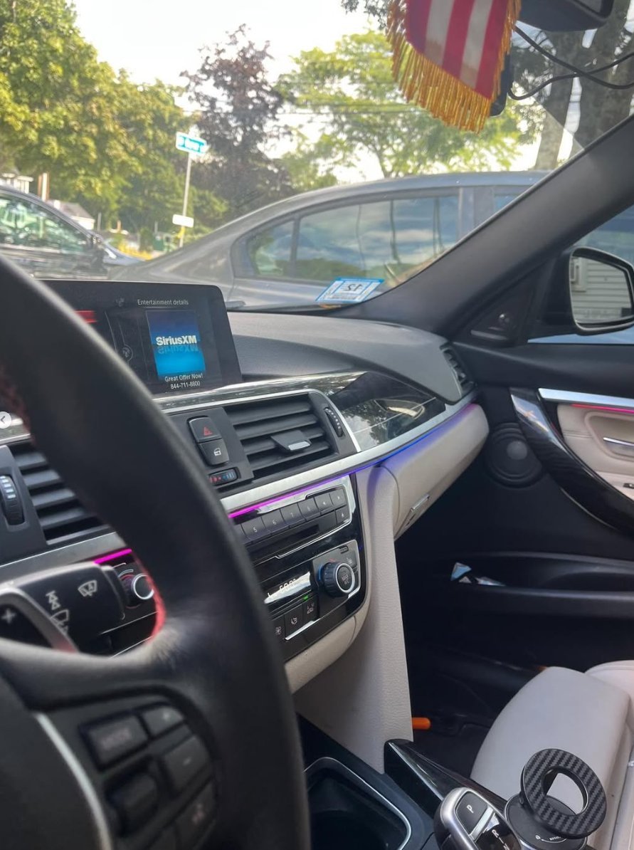 Interior view of car dashboard with steering wheel, touchscreen display showing SiriusXM, and two-tone black and white seats