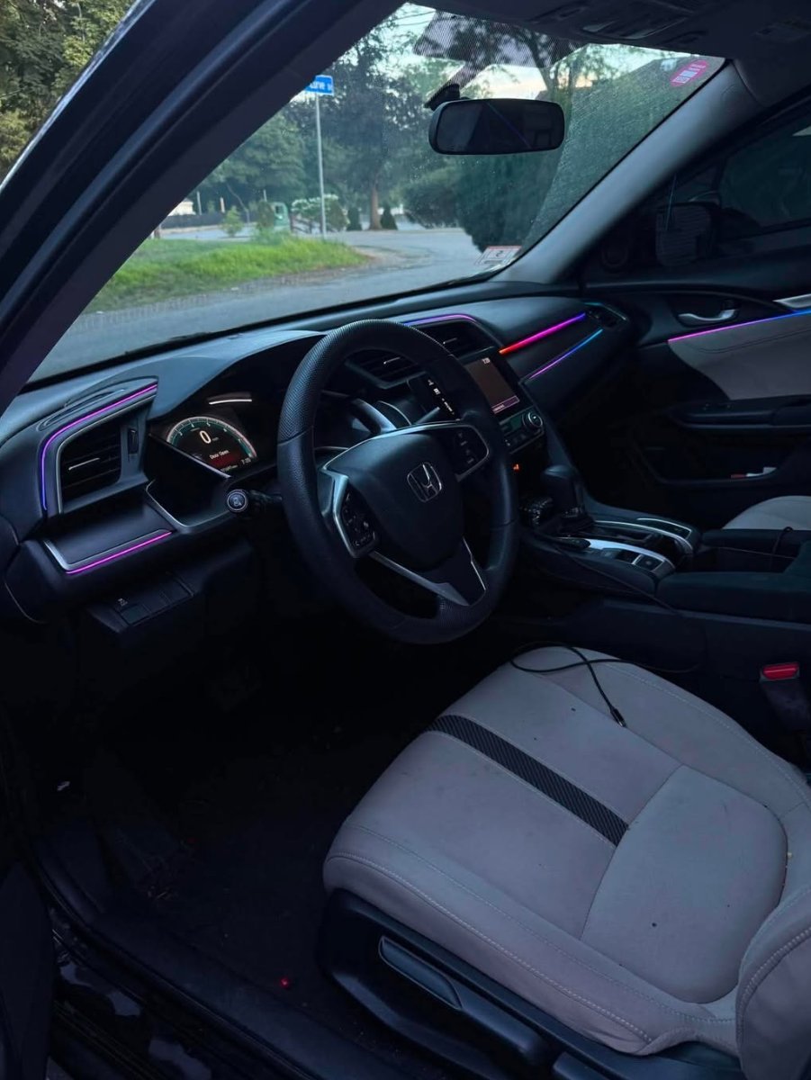 Interior view of Honda car with black steering wheel, purple ambient lighting, and gray seats parked on tree-lined street