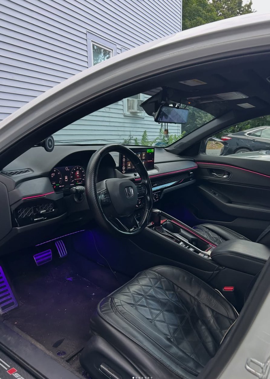 Interior view of a luxury car with black leather seats, steering wheel, dashboard with red accents, and purple ambient lighting