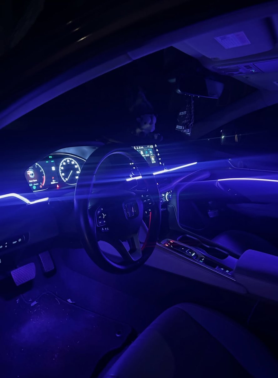 Car interior illuminated with blue neon lighting, showing steering wheel, dashboard, and glowing accent lights